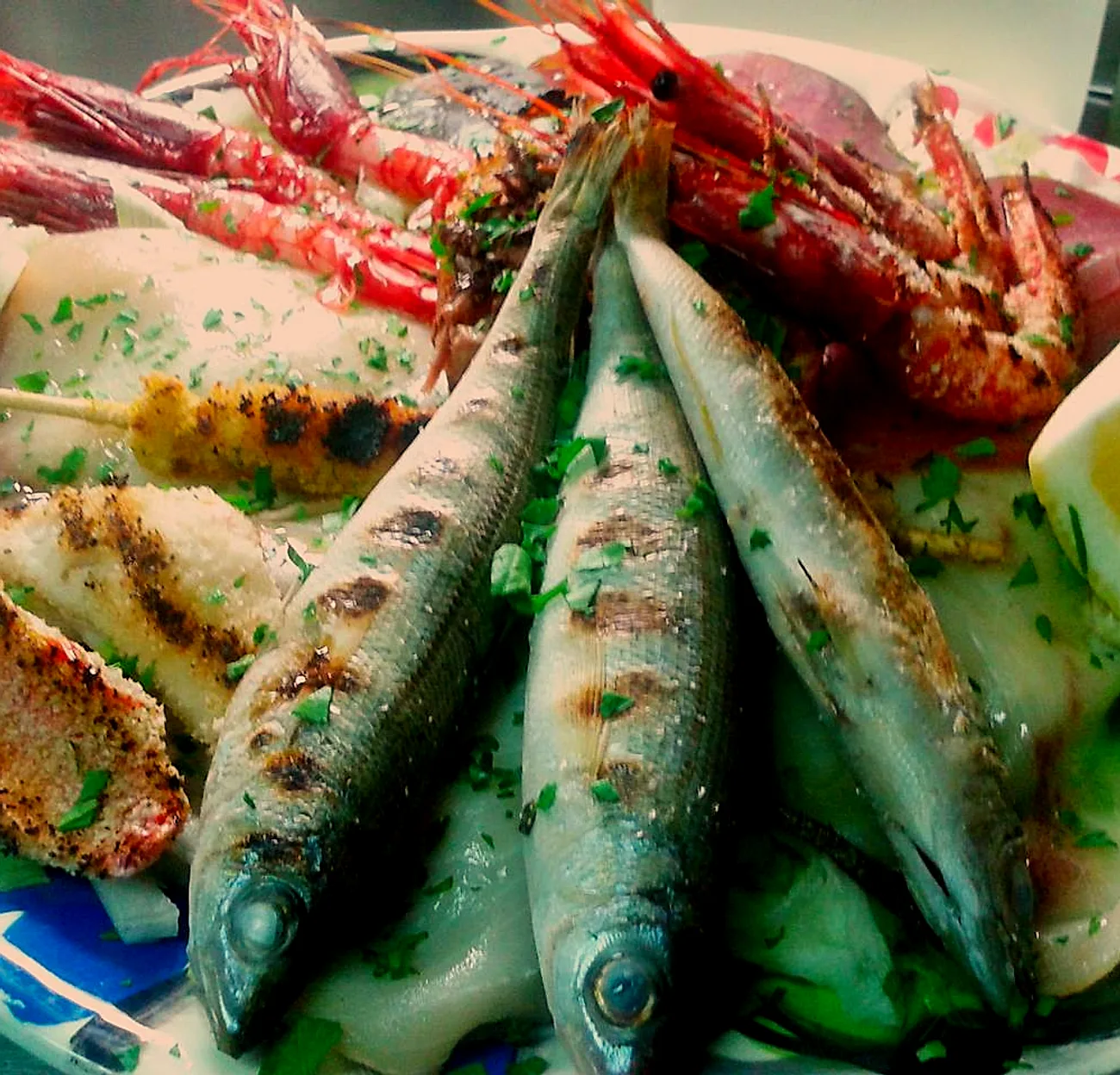 Un piatto di antipasto misto: gamberi rossi, pesce azzurro alla griglia, tonno crudo, calamaro e uno spicchio di limone