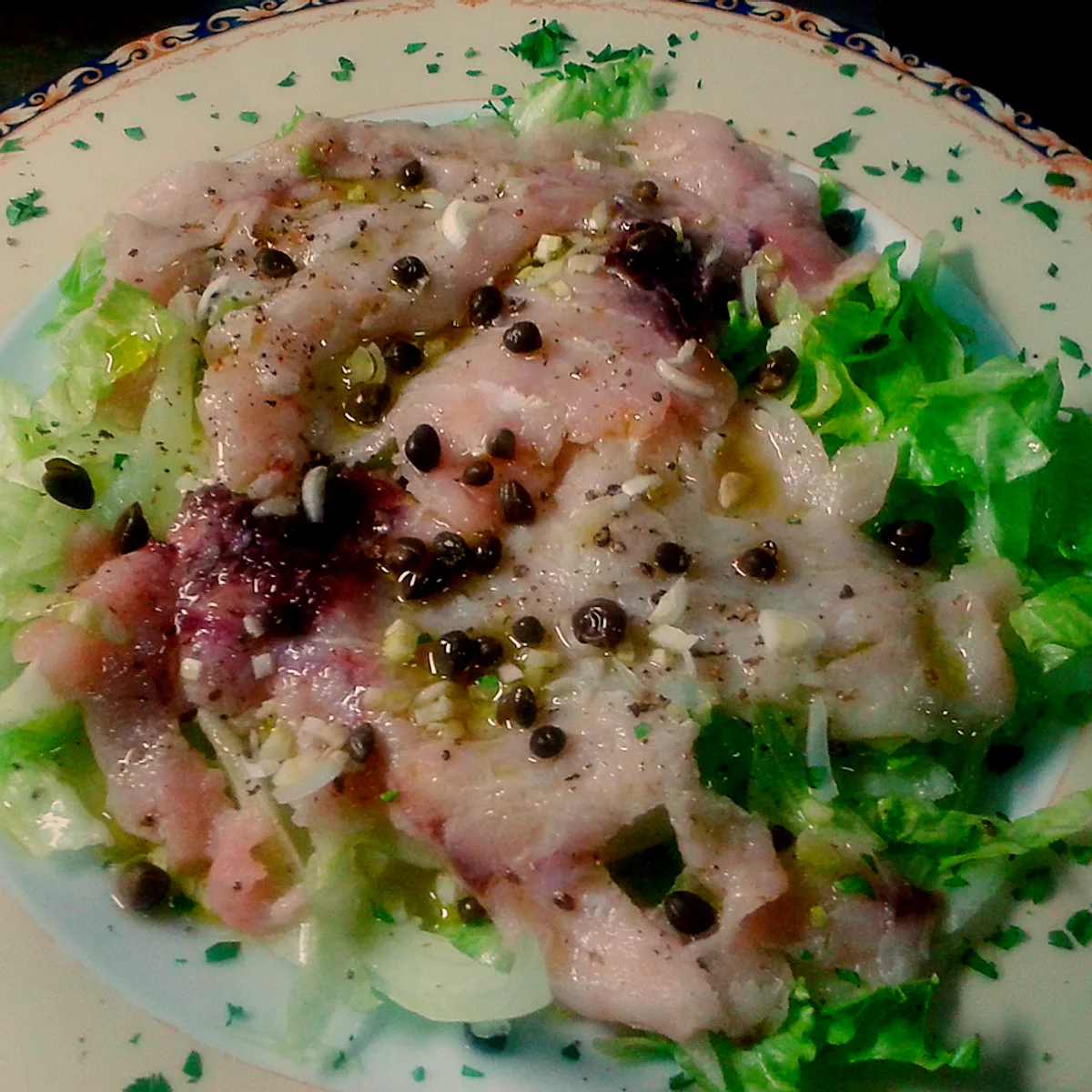 Pesce crudo affettato sottile con capperi, aglio e olio, su un letto di insalata