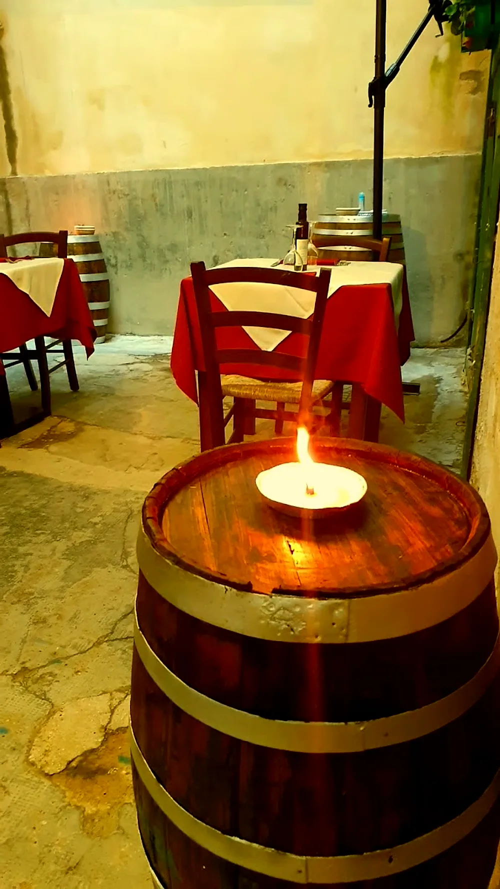 I tavoli apparecchiati fuori nel vicolo, con le tovaglie rosse e una candela accesa sopra una botte